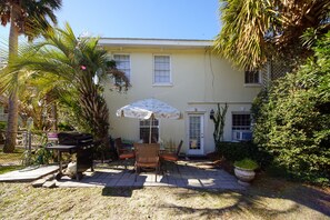 Una casa de dos pisos con un patio que incluye mobiliario exterior, una parrilla y un gran paraguas.