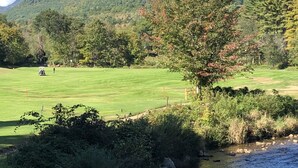 A golf course with a river in the foreground, surrounded by lush greenery and hills in the background. - The Gecko Inn - Shopping, Santas Village, Skiing, Hot Tub, hikes, families, pets (North Conway)