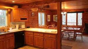 A wooden cabin kitchen with wooden cabinets, a dishwasher, a dining table with chairs, and a chandelier. - The Gecko Inn - Shopping, Santas Village, Skiing, Hot Tub, hikes, families, pets (North Conway)