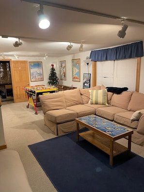 A cozy living room with a beige sofa, a coffee table, and a foosball table. There is a Christmas tree and wall art. - The Gecko Inn - Shopping, Santas Village, Skiing, Hot Tub, hikes, families, pets (North Conway)