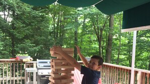 A wooden deck with a tall stack of wooden blocks, a grill, and red chairs. - The Gecko Inn - Shopping, Santas Village, Skiing, Hot Tub, hikes, families, pets (North Conway)