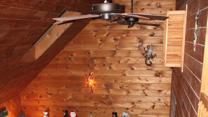 A cozy cabin interior with a fireplace, wooden walls, a ceiling fan, and a staircase leading to an upper level. - The Gecko Inn - Shopping, Santas Village, Skiing, Hot Tub, hikes, families, pets (North Conway)