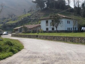 A rural road leading to a white house with a stone wall and a grassy area. - Village House in El Molin de Frieras / Posada de Llanes (Llanes)