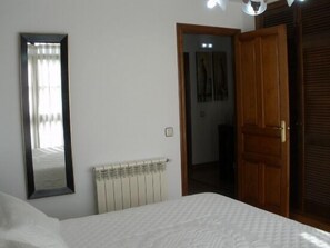 Un dormitorio con cama, un radiador, un espejo y una puerta que da a otra habitación.