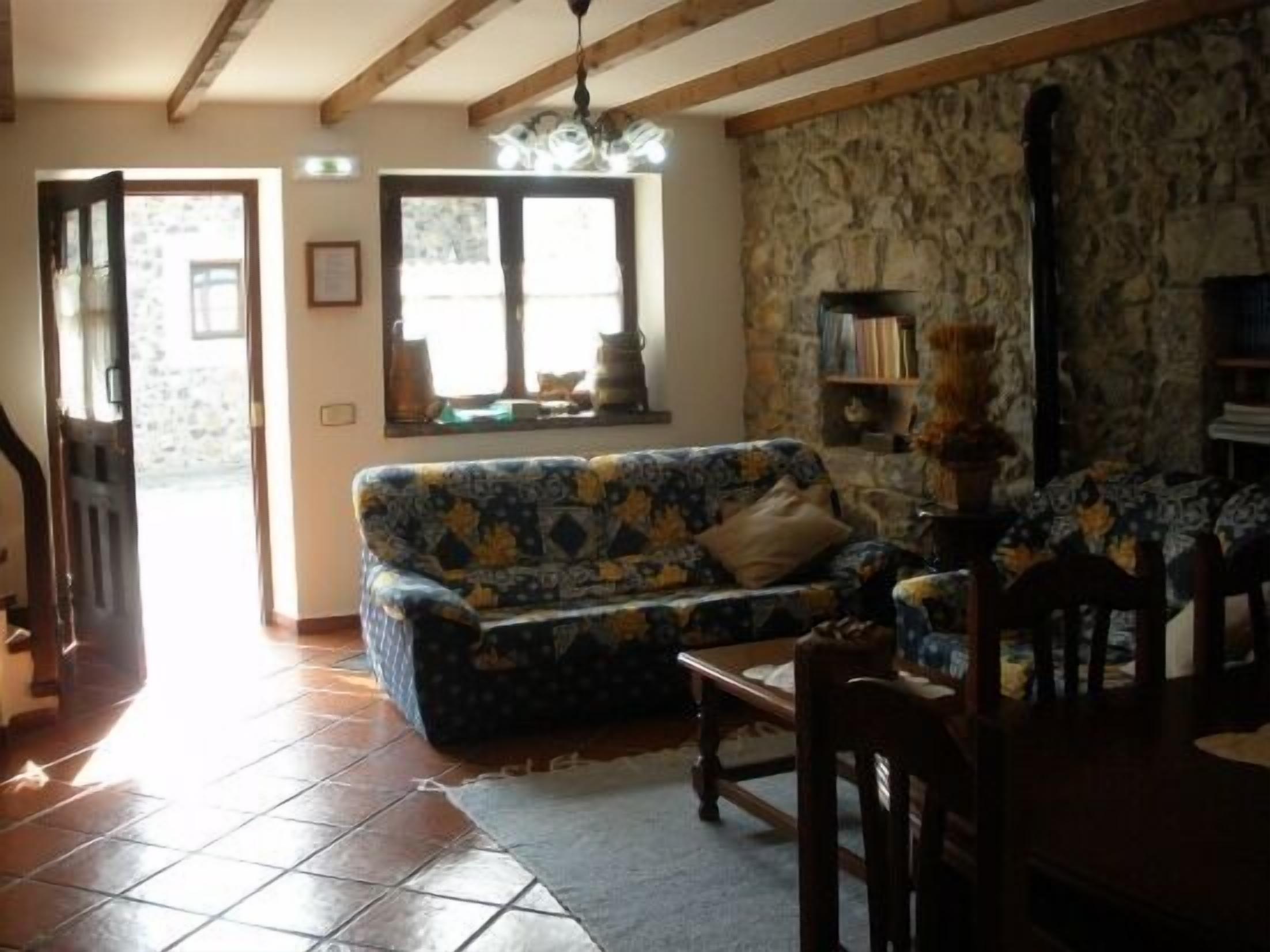 A cozy living room with a patterned sofa, a wooden dining table, and a stone wall.