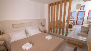 A hotel room with a large bed, a wooden partition, a desk, and a view of the sea through the windows.