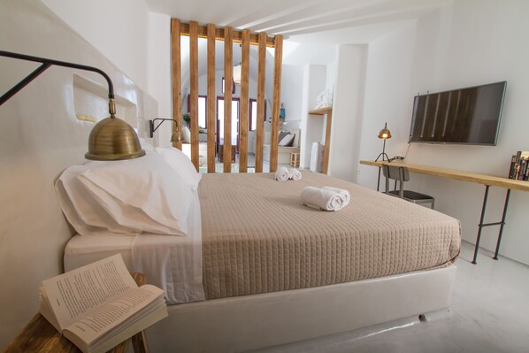 A modern hotel room with a large bed, a desk with a flat-screen TV, and a reading area with a book.