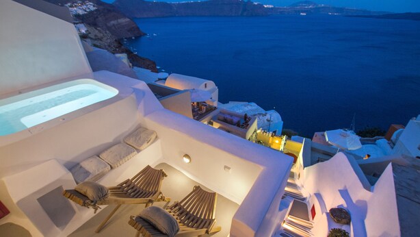 A sunlit outdoor seating area with lounge chairs and a built-in bathtub, overlooking a coastal landscape.