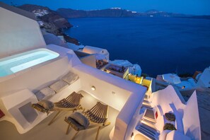 A sunlit outdoor seating area with lounge chairs and a built-in bathtub, overlooking a coastal landscape.