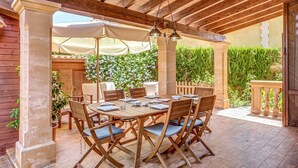 A covered patio with a wooden table and chairs, an umbrella, and a pergola with hanging lights.
