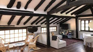 A room with exposed wooden beams, a white sofa, wicker chairs, a small round table, and a bookshelf. - Llanos De Penagos: Mansion - THE BUMBARO'S HOUSE (Llanos de Penagos)