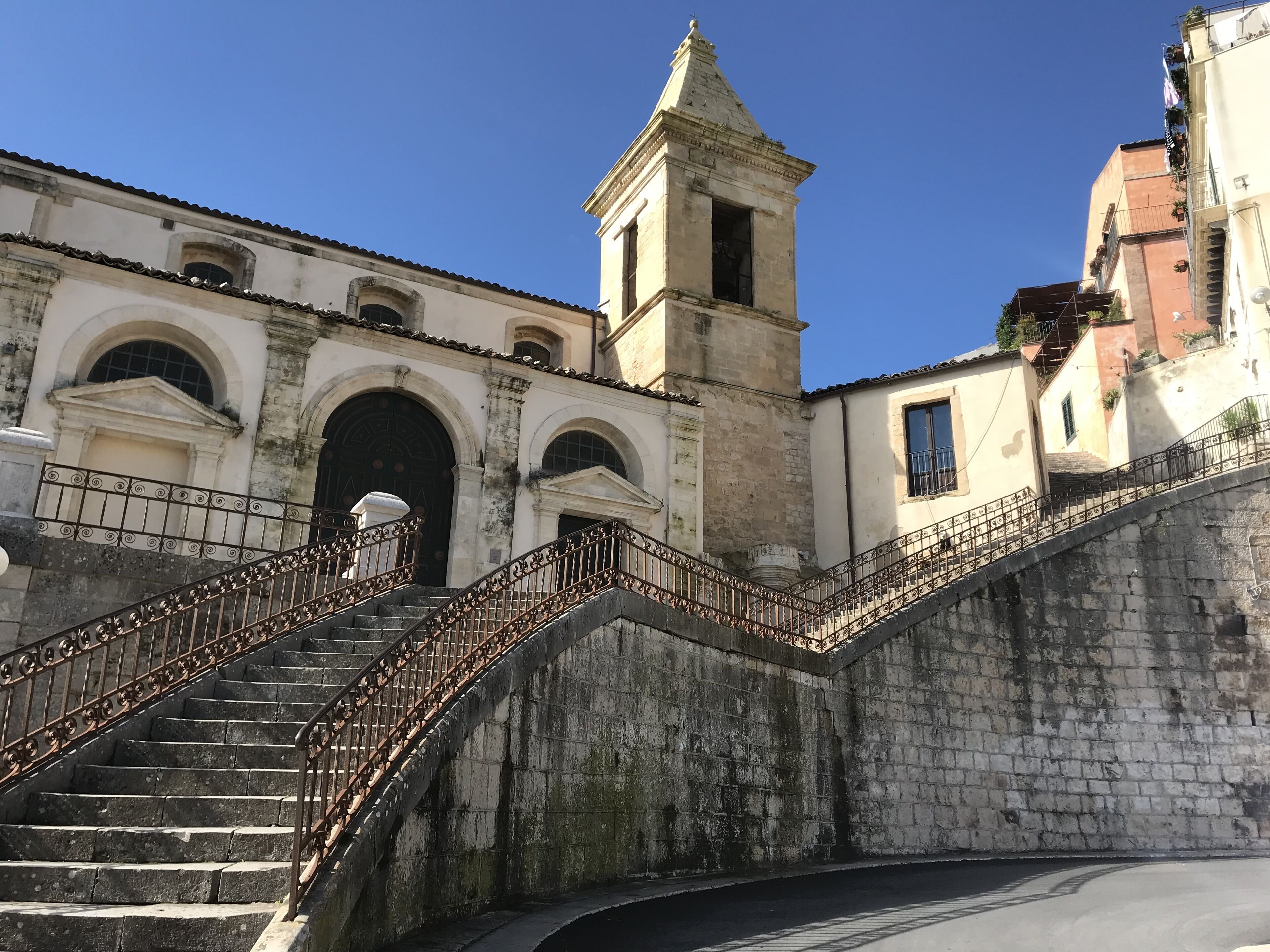 A historic building with a prominent staircase leading to an entrance, a bell tower, and a clear blue sky.