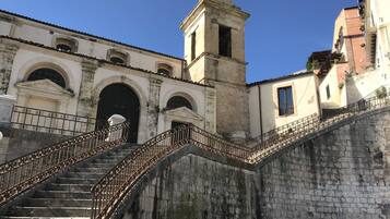 A historic building with a prominent staircase leading to an entrance, a bell tower, and a clear blue sky.
