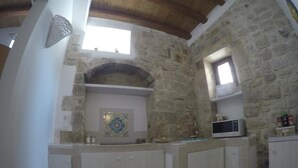 A kitchen with stone walls, white cabinets, a microwave, and a decorative tile backsplash.