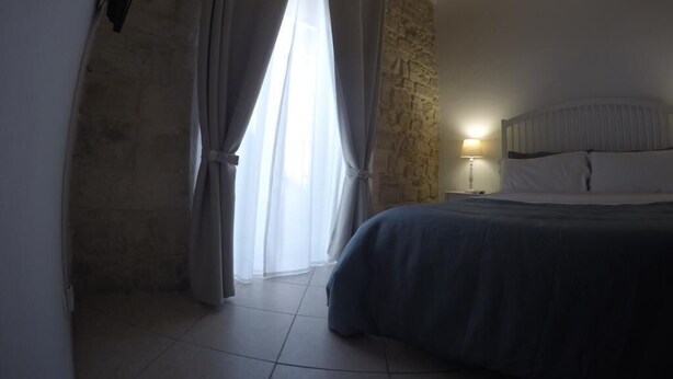 A bedroom with a bed, a stone wall, and a window with curtains.