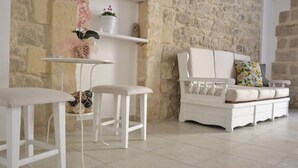 A room with a stone wall, a white sofa with a cushion, a small white table, and a chair.