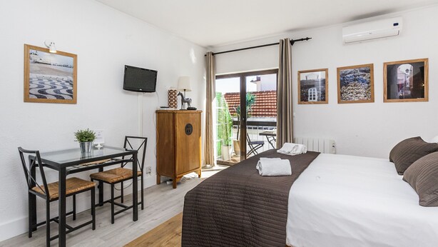 Habitación de hotel con cama, escritorio, sillas, televisor y vistas al exterior.