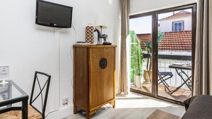 Una habitación con una televisión de pantalla plana montada en la pared, un mueble de madera, una mesa de comedor con sillas y un ventanal corredero que da a un área exterior con balcón.