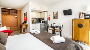 Habitación de hotel con cama, escritorio, silla, armario, televisor y kitchenette.