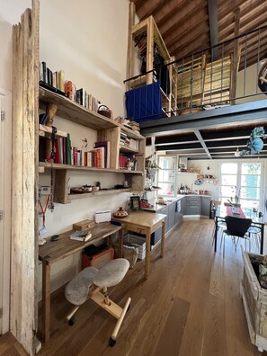 A spacious kitchen with wooden floors, a dining area with a table and chairs, and a loft with a blue curtain. - The Casina Lorenzana (Lorenzana)