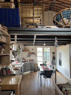 A spacious kitchen with wooden flooring, a dining area with a table and chairs, and a loft space with a hammock. - The Casina Lorenzana (Lorenzana)