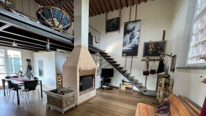 A spacious living area with a fireplace, wooden flooring, a dining table, and a staircase leading to an upper level.