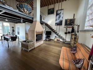 A spacious living area with a fireplace, wooden flooring, a dining table, and a staircase leading to an upper level. - The Casina Lorenzana (Lorenzana)