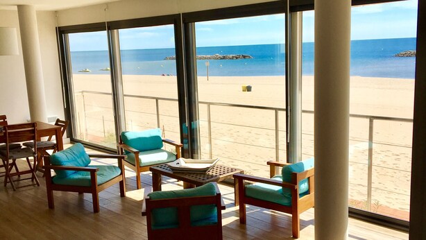 A spacious room with large windows overlooking a beach, wooden furniture, and a view of the ocean. - Beach house facing the sea (Valras-Plage)