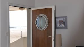 A room with a wooden door, a round window, a bed, a TV, and a beach view. - Beach house facing the sea (Valras-Plage)