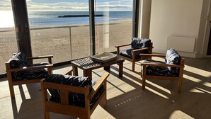 A room with large windows overlooking a beach, wooden furniture, and a tiled floor. - Beach house facing the sea (Valras-Plage)