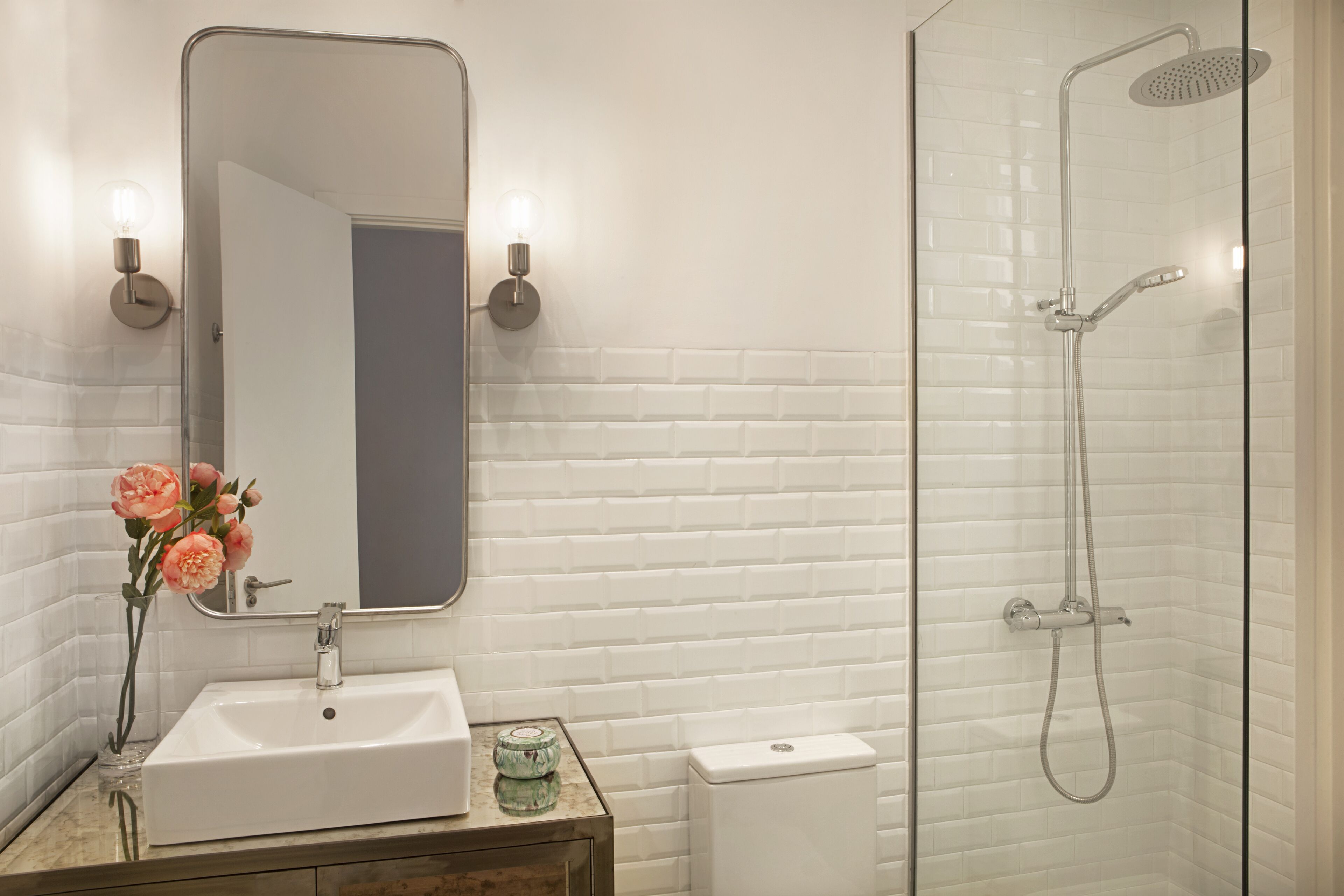 Un baño con lavamanos, espejo y ducha blancos.