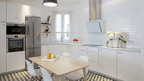 A modern kitchen with white cabinets, stainless steel appliances, a wooden dining table, and a pendant light. - 3Dorm / 3bathroom Apt-Gran Via Madrid Center-Terrace (Madrid)