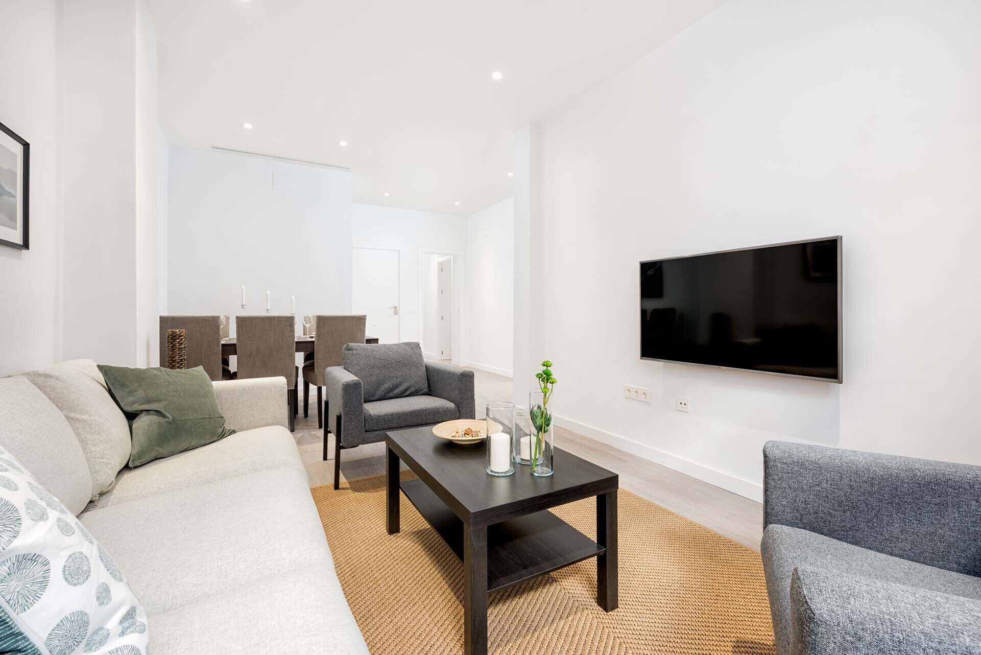 Un salon moderne comprenant un canapé, des fauteuils, une table basse et un téléviseur à écran plat fixé au mur.