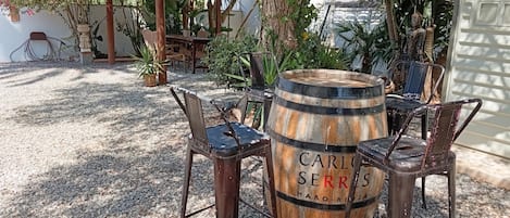 Zona d'estar a l'aire lliure rústica amb una taula de fusta en forma de cuba etiquetada "CARLOS SERRES HARO-RIJAJA" i cadires de metall al voltant.