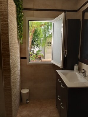 Une salle de bain avec une fenêtre, un lavabo, un miroir et une poubelle.