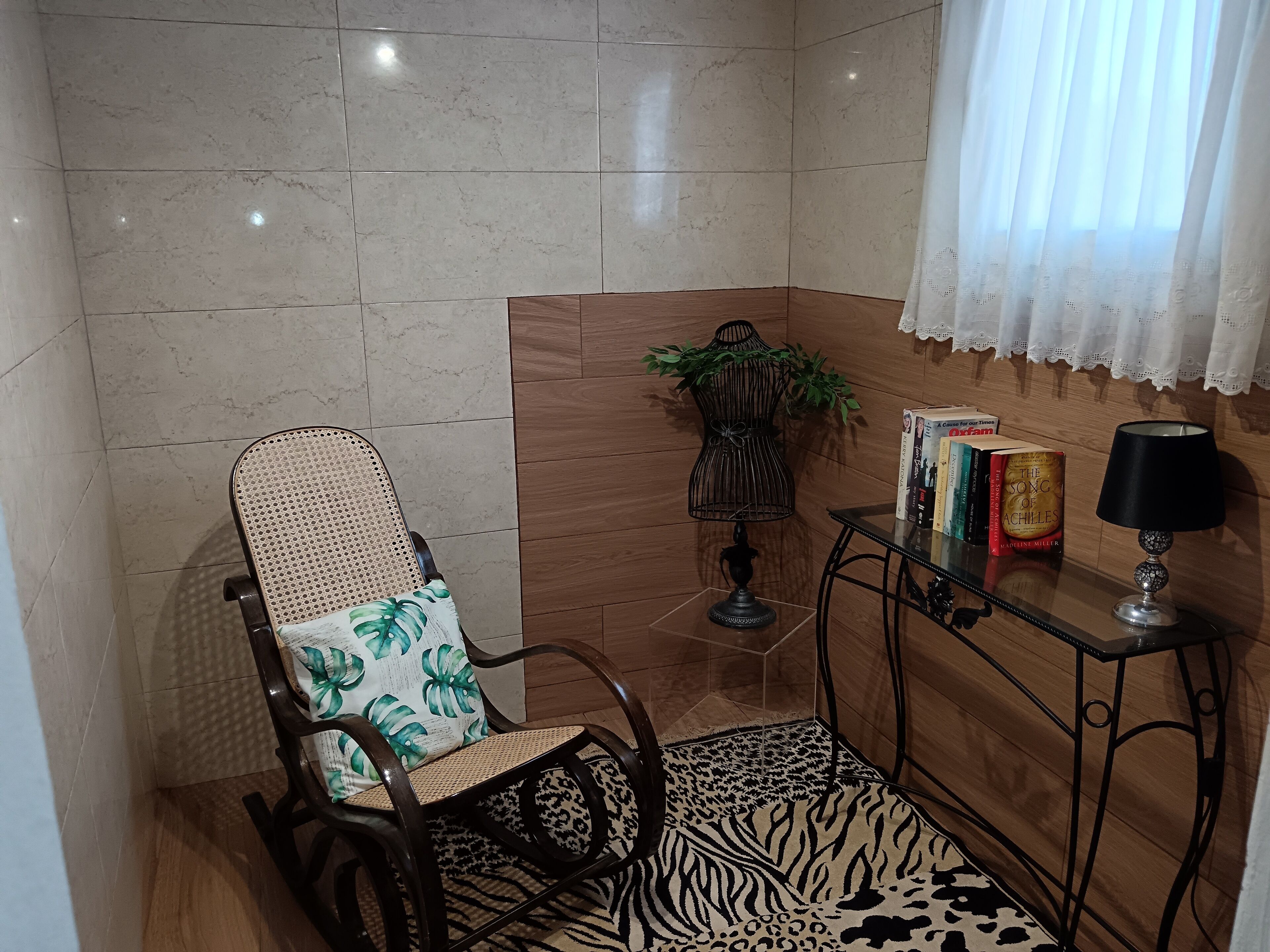 A corner room with a wooden chair, a small table with books, a lamp, and a plant.