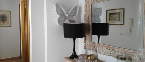 A room with a large mirror, a dresser with drawers, a telephone, and a wall-mounted lamp.