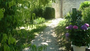 A gravel path leading through a garden with dense foliage and a stone building in the background. - Beautiful Old Bastide with private pool and heated Nordic bath, near Montcuq (Montcuq-En-Quercy-Blanc)