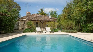 A pool area with two lounge chairs, a stone building with a tiled roof, and lush greenery surrounding the space. - Beautiful Old Bastide with private pool and heated Nordic bath, near Montcuq (Montcuq-En-Quercy-Blanc)