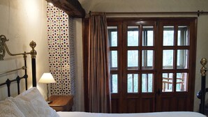Une chambre à coucher avec un lit, une table de chevet, une lampe, une fenêtre avec des rideaux et un mur à motifs.