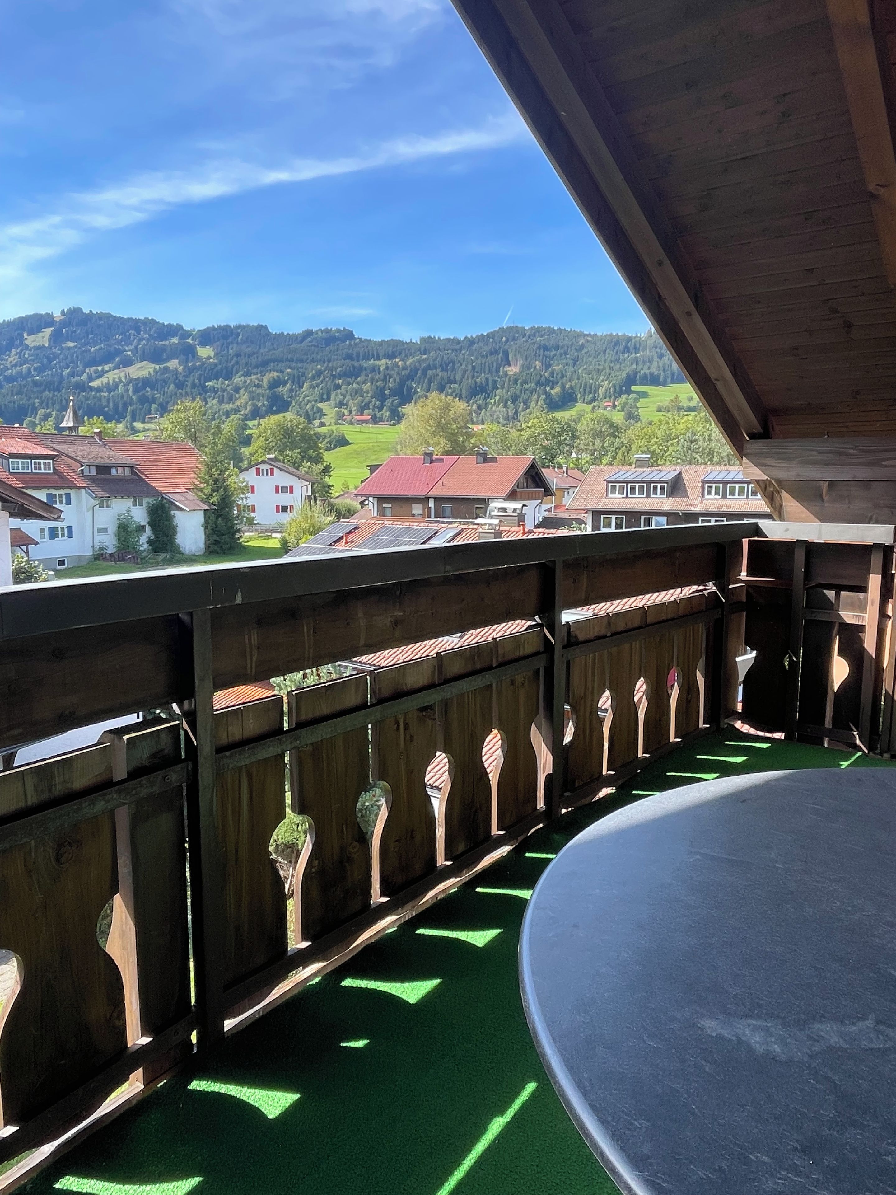 A balcony with a view of a village, wooden railing, and a green artificial turf floor.