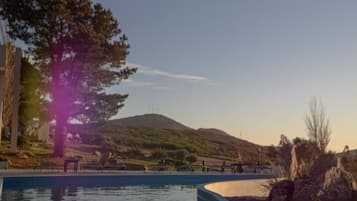 A swimming pool with a view of a hill and a tree.