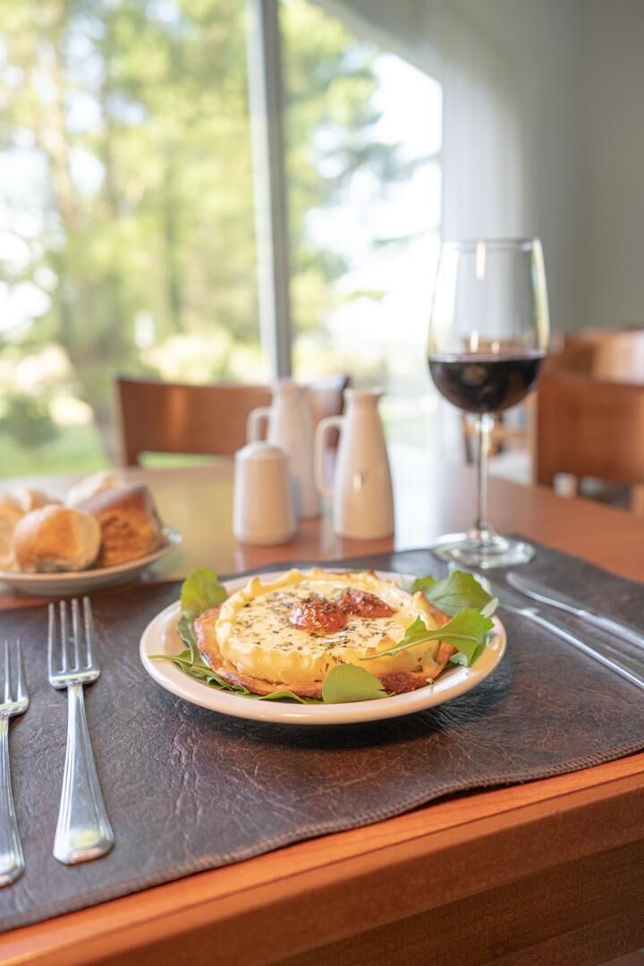 Una mesa de comedor con un plato de comida, una copa de vino tinto y salero y pimentero.