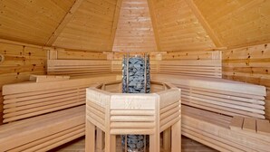 A sauna with wooden benches arranged in a semi-circle, a central stone heater, and a sloped wooden ceiling. - Exclusive Country house Seewald - quiete area, Whirlpool, Sauna, large garten, bbq, wifi (Seewald)