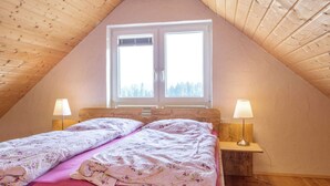 A cozy attic bedroom with a sloped wooden ceiling, a large window with a view of trees, a bed with floral bedding, and two bedside lamps. - Exclusive Country house Seewald - quiete area, Whirlpool, Sauna, large garten, bbq, wifi (Seewald)