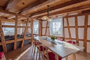 A rustic interior with exposed wooden beams, a long dining table, and a cozy seating area.