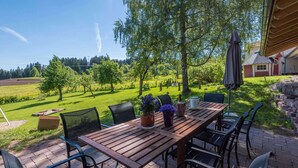 An outdoor patio with a wooden table and chairs, a potted plant, and a view of a green landscape with trees and a building in the background. - Exclusive Country house Seewald - quiete area, Whirlpool, Sauna, large garten, bbq, wifi (Seewald)