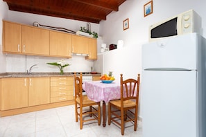 Una cocina con armarios de madera, un refrigerador blanco, una mesa de comedor con sillas y un microondas sobre la encimera.