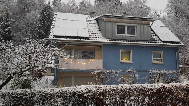 Ein zweistöckiges Haus mit Dachgaube, einer sichtbaren Garage und einer verschneiten Landschaft.