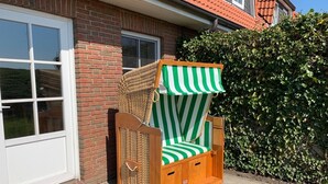 A wicker chair with a striped canopy, positioned outside a brick building with a white door and a tiled roof. - Komf. Apartment, 5 pers., 3 bedrooms, 2 bathrooms, near Sankt Peter-O. , right on the dike (Tönning)